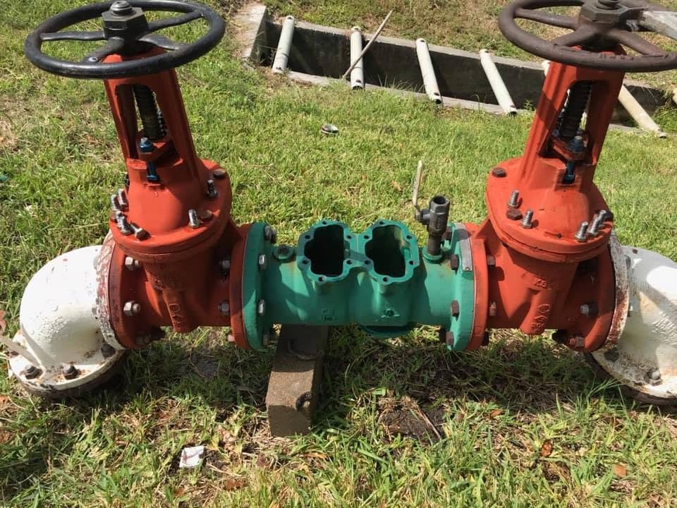 Certified technician performing a backflow assembly test on an outdoor pipe setup